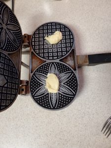 Italian Anise Pizzelles Two balls of cookie dough sitting on a hot pizzelle cookie iron.