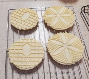 Italian Anise Pizzelles Several round flat cookies with decorative imprints cooling on a rack.