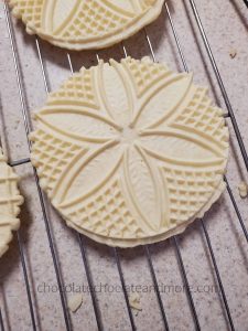 Italian Anise Pizzelles round Italian Anise Pizzelles waffle cookies cooling on a wire rack. there is a delicate flower pattern baked into the cookies.