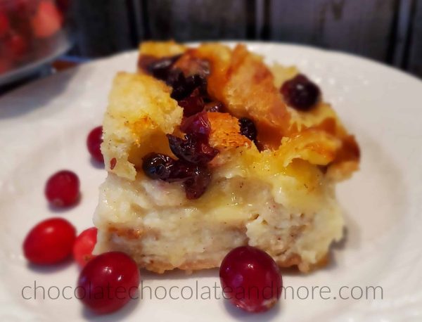 A slice of cranberry brie pudding on a white plate surrounded by fresh cranberries.