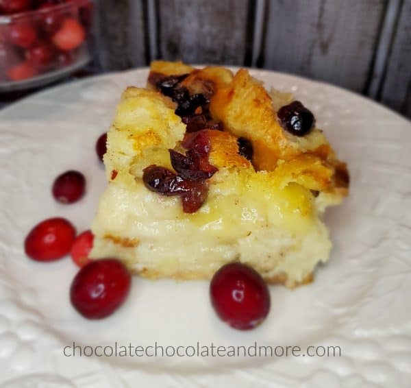 A slice of cranberry brie bread pudding on a white plate with fresh cranberries.