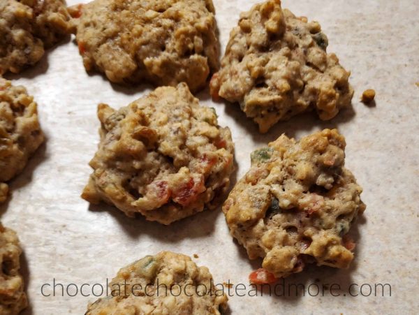 Several fruitcake cookies sitting on a counter with chunks of red and green fruit showing through the dough.