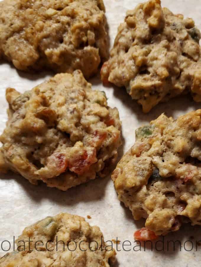 Several fruitcake cookies sitting on a counter with chunks of red and green fruit showing through the dough.