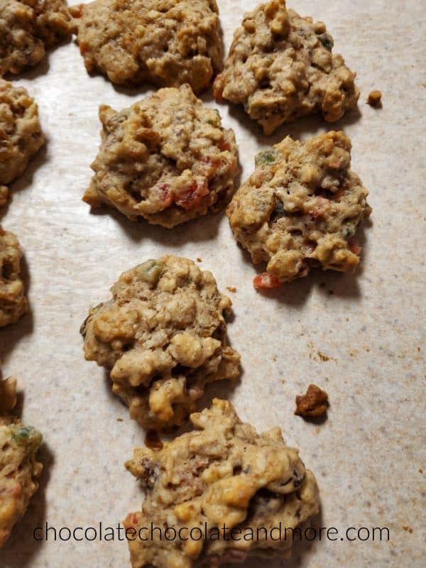 Several fruitcake cookies sitting on a counter with chunks of red and green fruit showing through the dough.