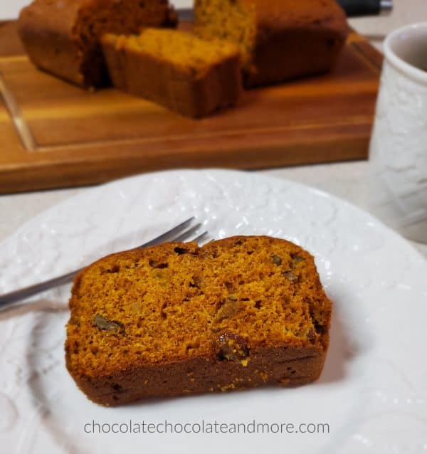 a slice of pumpkin bread on a white plate with a sliced loaf on a wooden cutting board
