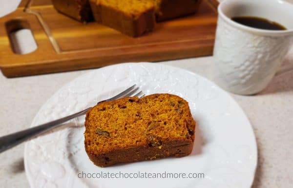 a slice of pumpkin bread on a white plate with a cup of coffee and a sliced loaf on a wooden cutting board