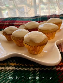 6 Eggnog Cream Cheese Cupcakes sitting on a green, red, and white blanket with a white lace curtain in the background.