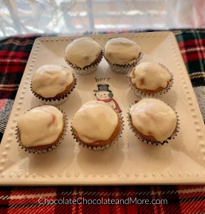 7 regular Eggnog Cream Cheese Cupcakes sitting on a square plate with a snowman on it on top of a red, green, and white plaid blanket with a white lace curtain in the background.