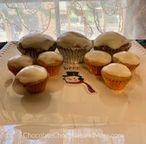 3 regular Eggnog Cream Cheese Cupcakes and 6 mini cupcakes sitting a a square plate with a snowman in the middle with a white lace background.