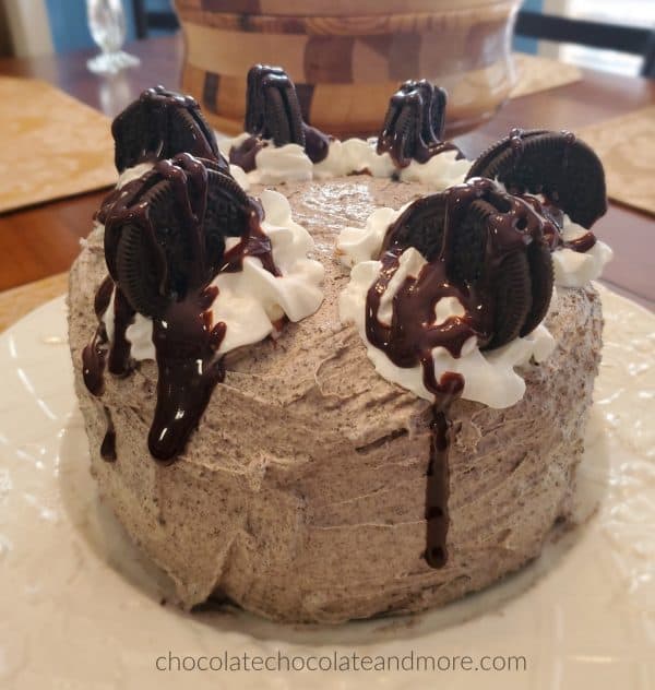 a whole oreo cake covered with buttercream frosting and topped with oreos and chocolate syrup