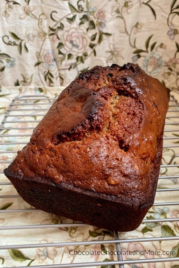 A loaf of banana nut bread sitting on a metal cooling rack with a brown floral background.
