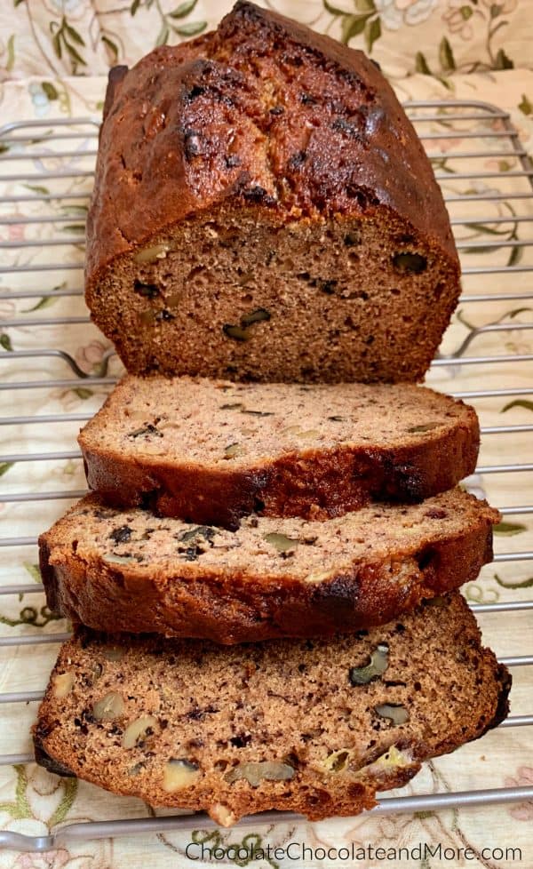 Half a loaf of Banana Nut Bread sitting behind 3 slices of banana nut bread on a metal cooling rack with a brown floral background.