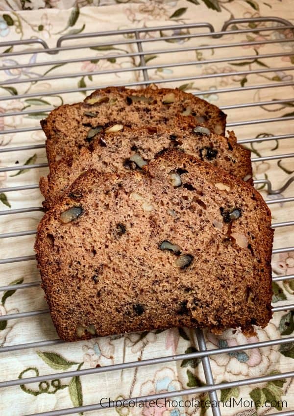 3 slices of banana nut bread sitting on a metal cooling rack with a brown floral background.