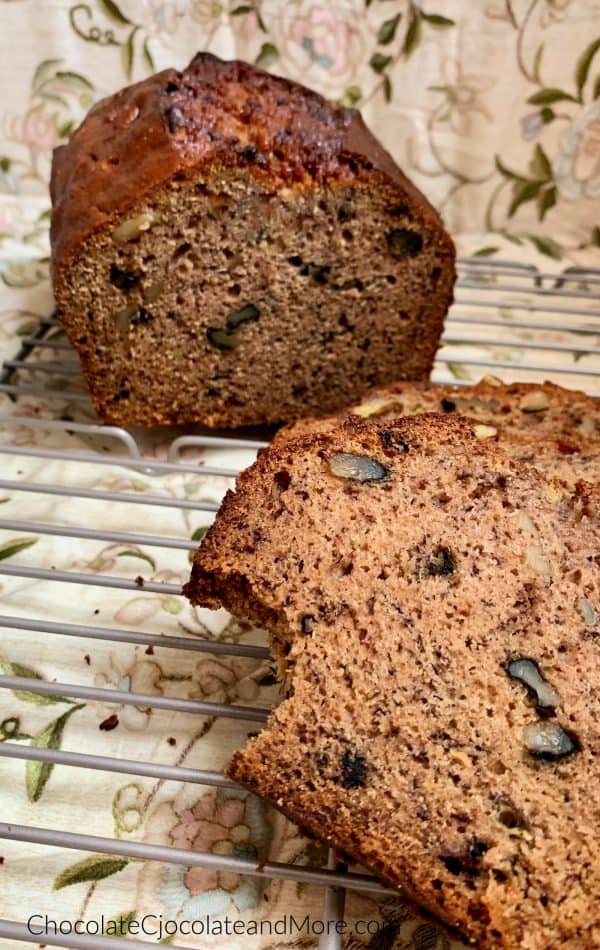 Half a loaf of banana nut bread sitting behind a slice of banana nut bread with a bite taken out sitting on a metal cooling rack with a brown floral background.
