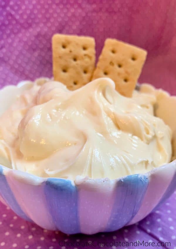 A bowl of 3-Ingredient Cheesecake Dip with 2 graham crackers sticking out with a purple and white polka dot background.