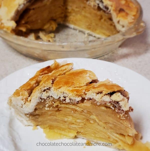 a slice of apple pie with the rest of the pie in the background