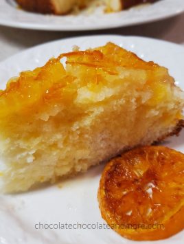 a slice of yellow cake topped with sliced oranges next to a candied orange slice