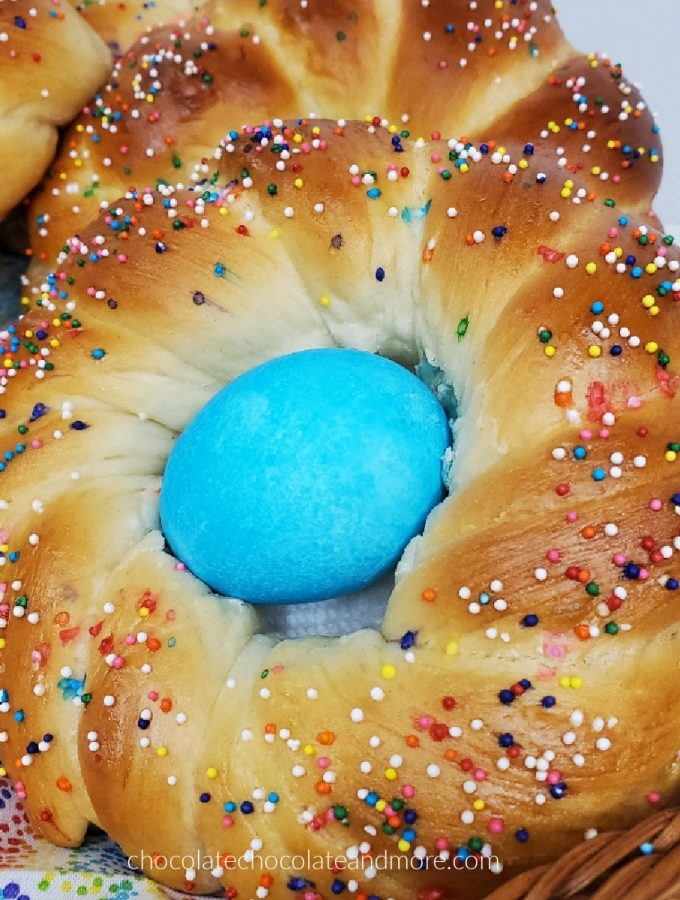 A twisted Italian Easter Bread covered in colorful sprinkles and a blue Easter egg.