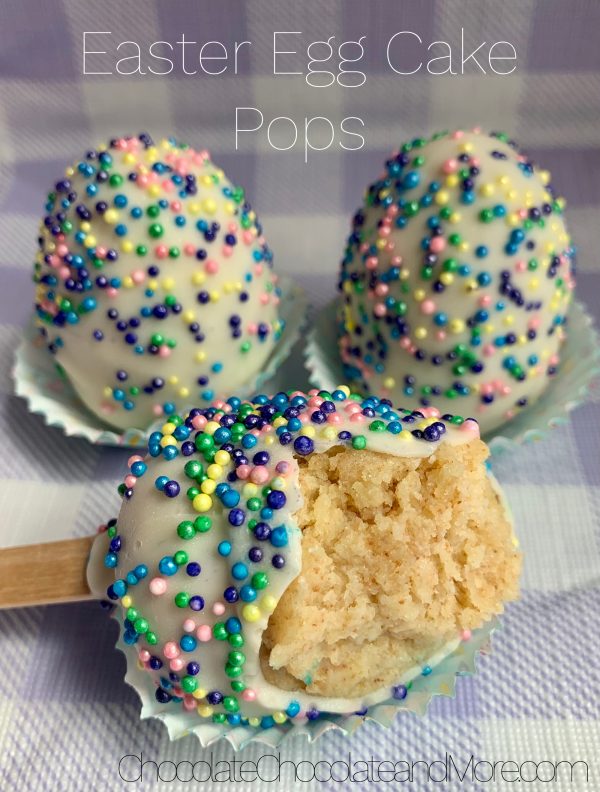 3 Easter egg Cake Pops (one with a bite taken out) sitting in mini cupcake holders on a purple and white plaid background.