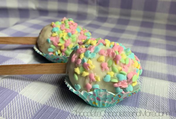 2 Easter Egg Cake Pops sitting in mini cupcake holders on a purple and white plaid background.