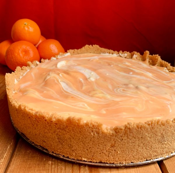 A whole Orange Creamsicle Swirl Cheesecake sitting in front of a red background.