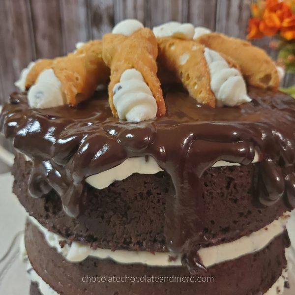 a chocolate layer cake dripping with chocolate frosting and topped with cannolis