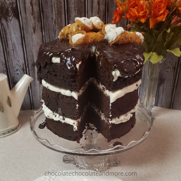 A huge three layer chocolate cake layered with cannoli filling and topped with several cannolis