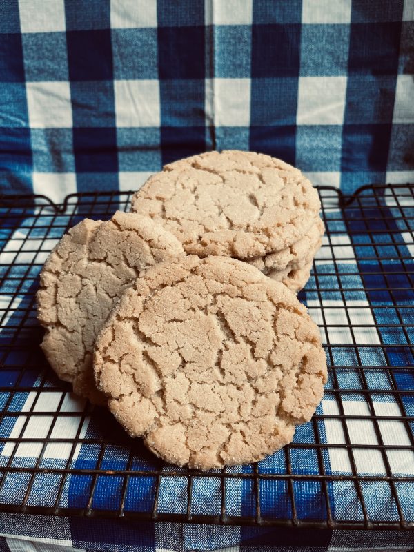 a stack of Cream Cheese Frosted Sugar Cookies sitting on a cooling rack on a blue and white checkered background.