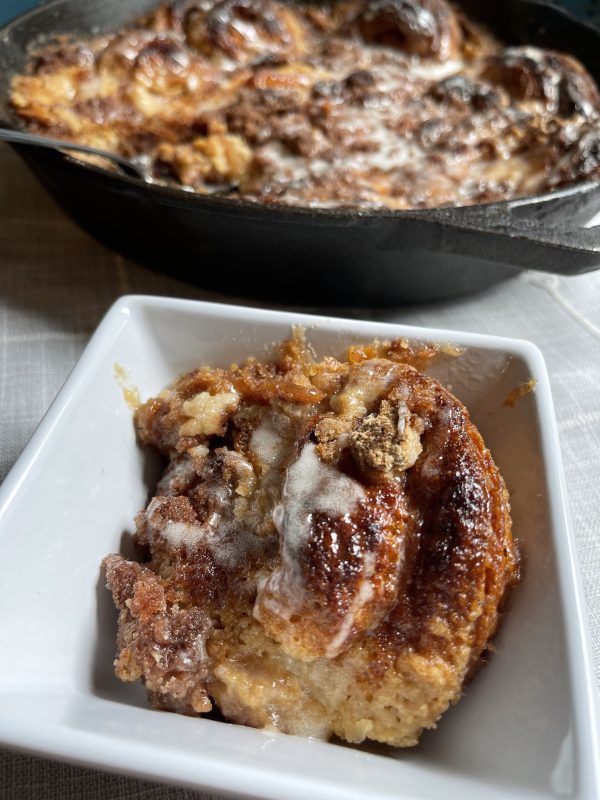Some of the Cinnamon Roll Dessert Casserole in a dish in front of the skillet.