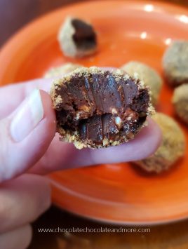 a partially eaten truffle being held above an orange plate of truffles