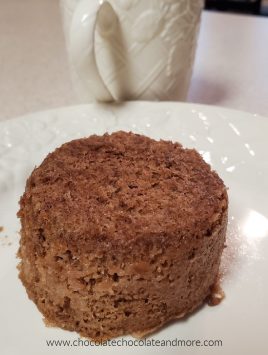 a small round chocolate cake on a plate with a mug in the background