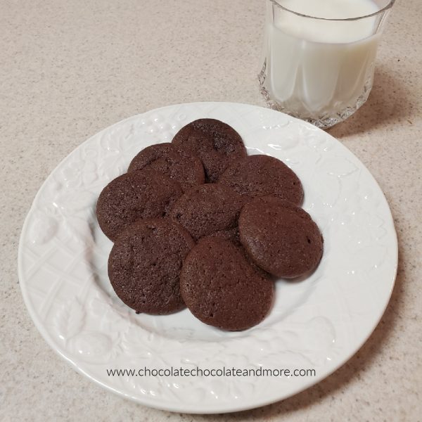 Chocolate Drop Cookies several dark chocolate cookies on a white plate next to a glass of milk