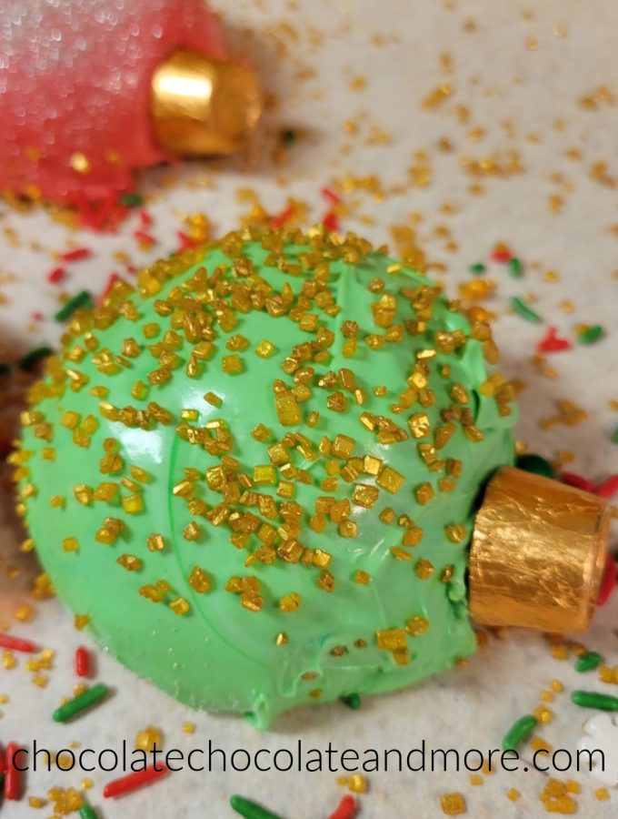 a green Christmas ornament shaped cupcake covered in gold sprinkles