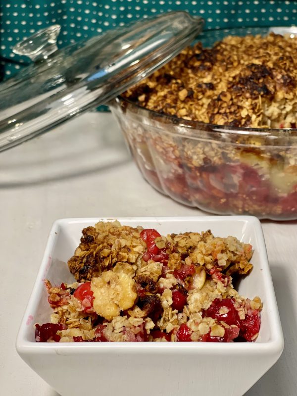 Granny's Cranberry Apple Pecan Casserole scooped into a tiny bowl witht eh casserole dish in the back.