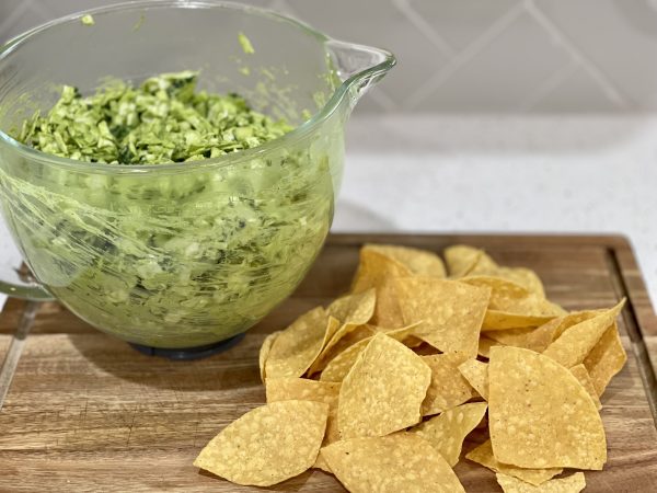 Green Goddess Salad in a glass bowl on a Wood cutting board wit some chips next to it.