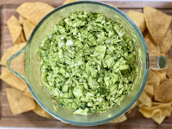 Green Goddess Salad in a glass bowl on a Wood cutting board wit some chips next to it.