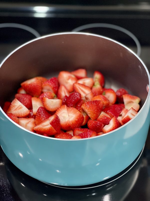 Cut up strawberries in a pot on the stove.