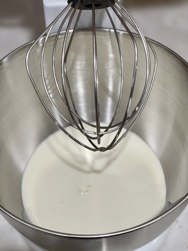 Heavy cream in the stand mixer bowl with the whisk attachment attached.