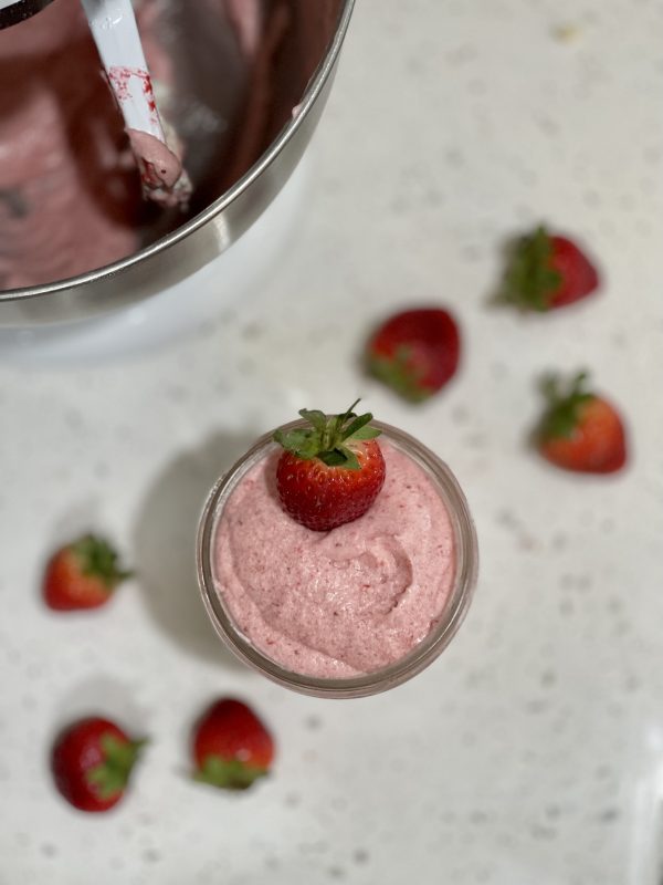 Overhead view of Homemade Strawberry Frosting in a mason jar with a mixer in the back and starwberries laying next to it.