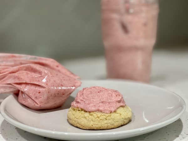 Homemade Strawberry Frosting on a sugar cookie with the filled mason jar behind it.