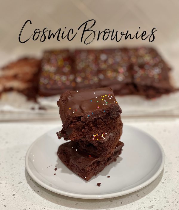 Cosmic Brownies stacked on a plate in front of a tray of Cosmic Brownies.