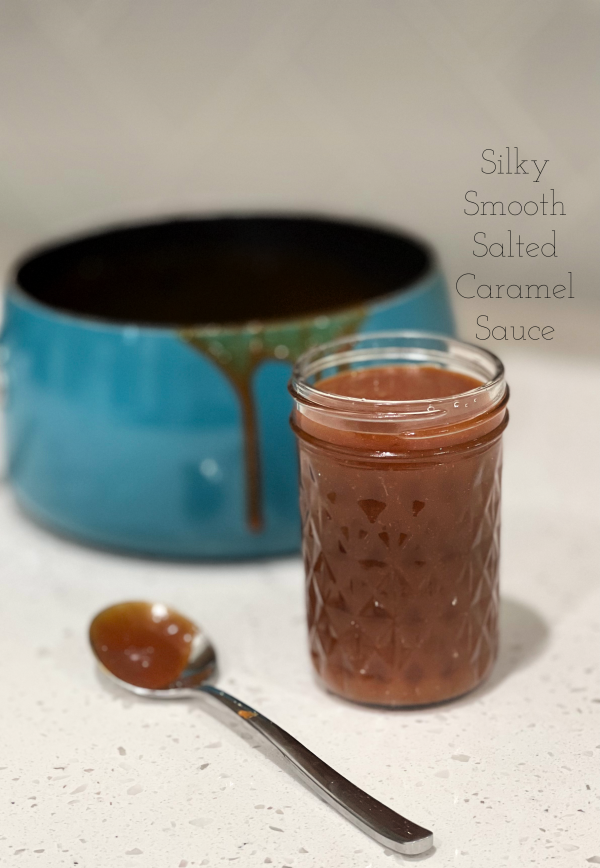 Silky Smooth Salted Caramel Sauce in a jar next to a spoon and in front of a saucepan