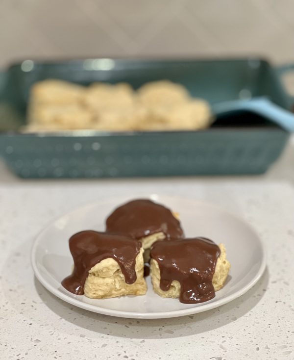 Chocolate Gravy Covered Buttermilk Biscuits 3 Chocolate Gravy Covered Buttermilk Biscuits on a white plate with the baking dish of biscuits behind it