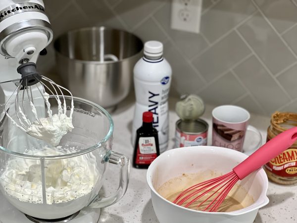 Whipped cream in a stand mixer, and other ingredients whisked together in a medium white bowl.