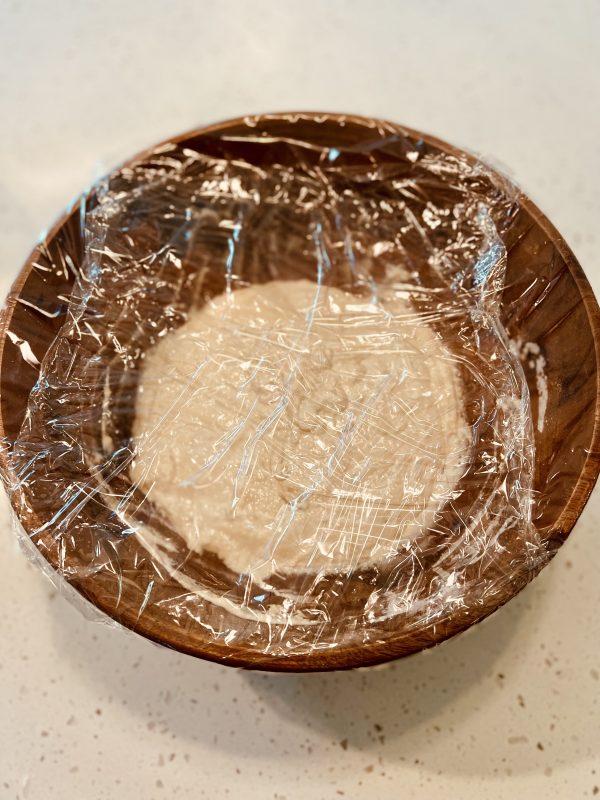 dough in a large wooden bowl with the cling wrap on before rising
