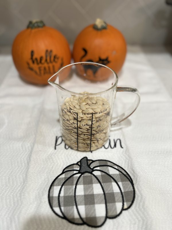 washed pumpkin seeds in a glass measuring cup and two pumpkins sitting behind it.