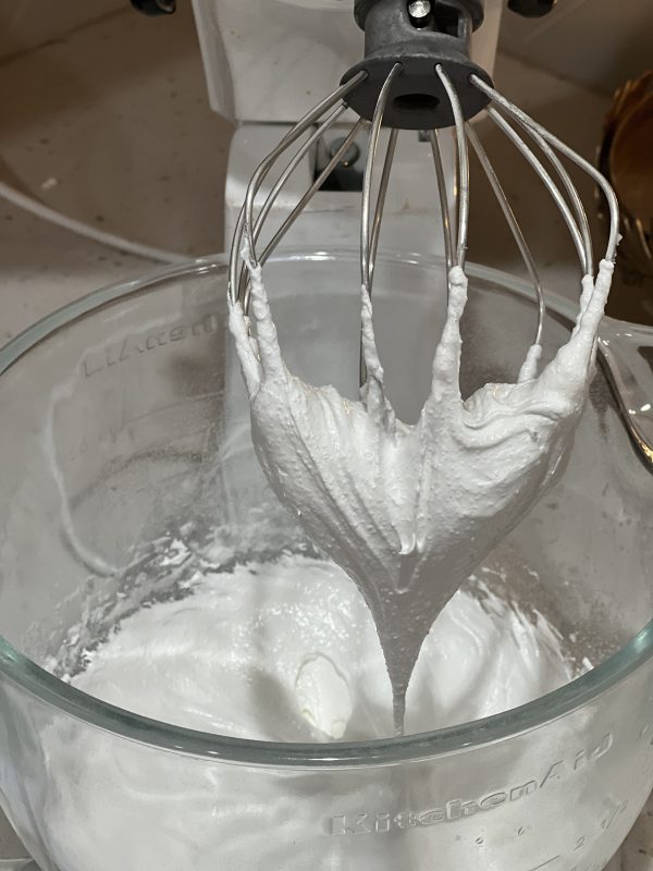 Egg whites after a stiff peak has formed in a glass mixing bowl