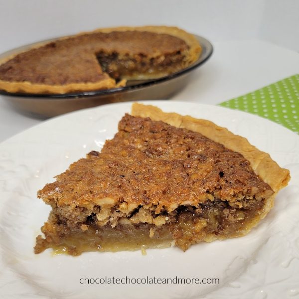 a slice of pecan pie on a white plate in front of a cut pie.